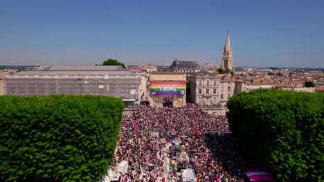 Crowded-street-pulse-with-vibrant-Gay-Pride-parade,-adorned-by-colossal-rainbow-flag