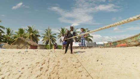 Young-men-pull-fishing-net-by-rope-to-sunny-sand-beach-in-Moree,-Ghana