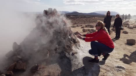 Touristin-Wärmt-Sich-Mit-Rauchender-Fumarole-Im-Geothermischen-Gebiet-Námafjall-Hverir-Im-Nordosten-Islands-Auf