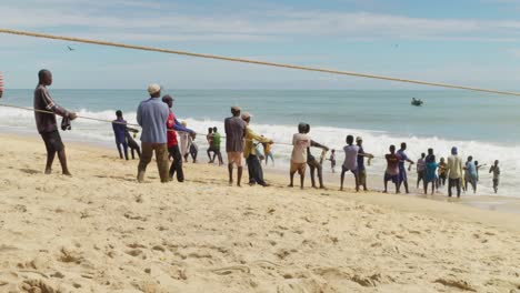 Los-Hombres-Tiran-De-Cuerdas-A-La-Red-De-Pesca-Desde-El-Mar-Hasta-La-Playa-De-Arena-En-Moree,-Ghana