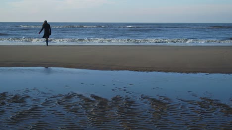 Weibchen-An-Einem-Winterlichen,-Windigen-Strand,-Der-In-Echtzeit-Wartet-Und-In-Der-Hand-Läuft