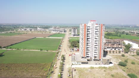 Toma-Aérea-De-Un-Dron,-La-Cámara-Del-Dron-Va-Hacia-El-Frente-Donde-Se-Está-Llevando-A-Cabo-La-Construcción-Del-Complejo-Y-Hay-Casas-Residenciales-Alrededor