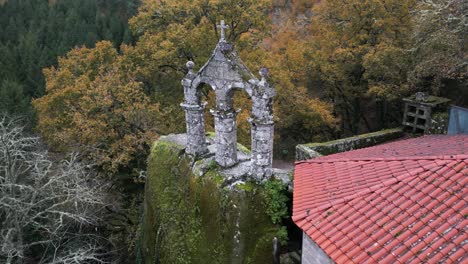 Toma-Aérea-De-Un-Antiguo-Monasterio-Rodeado-De-árboles-Y-Naturaleza-Con-Una-Cruz-Cristiana-En-La-Parte-Superior