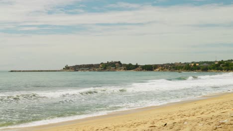 Waves-wash-over-sand-beach-by-cape-at-coast-of-Ghana,-woman-walks-by