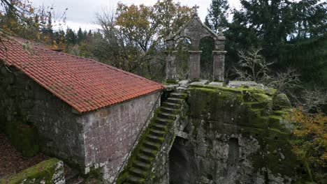 Aerial-drone-shot-of-a-beautiful-old-building-showing-the-exterior-stairs,-a-roof-and-a-high-Christian-cross-of-a-monastery