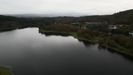 Wunderschöne-Luftdrohnenaufnahme-Der-Landschaft-Des-Cachamuiña-Stausees-An-Einem-Bewölkten-Tag,-Umgeben-Von-Bäumen