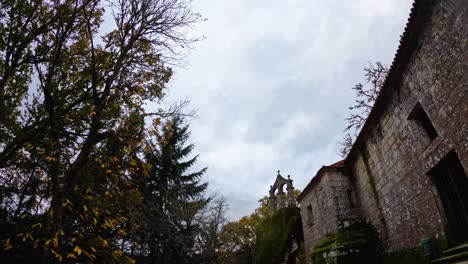 Hermoso-Timelapse-Del-Cielo-Gris-Nublado-Rodeado-De-árboles,-Naturaleza-Y-Una-Antigua-Construcción-De-Piedra-Con-Una-Cruz-Cristiana-Encima