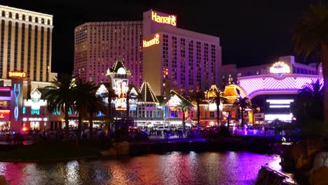 Colorida-Vista-Nocturna-Del-Hotel-Y-Casino-Harrah&#39;s,-Repleta-De-Gente-Y-Luces-De-Neón-Reflejándose-En-El-Agua