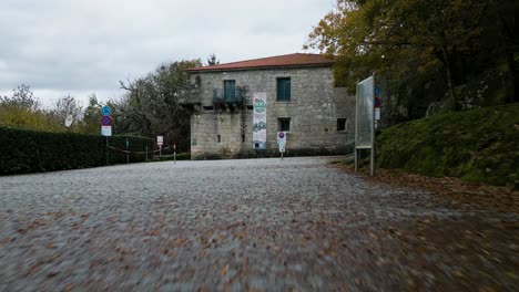 Frontalaufnahme-Des-Alten-Klosters-San-Pedro-De-Las-Rocas-Mit-Rotem-Dach,-Fenstern,-Einem-Langen-Schild-Davor-Und-Zäunen,-Die-Den-Durchgang-Verhindern,-Umgeben-Von-Wunderschönen-Bäumen-Und-Natur