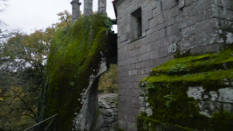 Narrow-entrance-between-rocks-and-gray-walls-with-slats-of-a-majestic-and-old-construction-surrounded-by-trees-and-nature