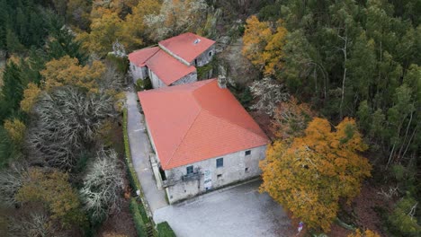 Circular-aerial-drone-shot-of-a-beautiful-old-construction-with-roll-roofs-surrounded-by-trees-and-nature