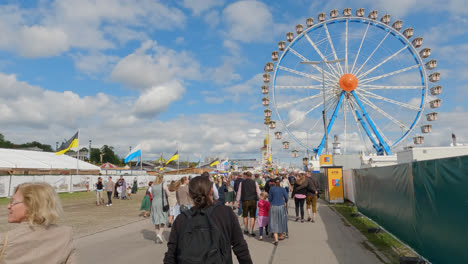 Gente-Caminando-En-El-Recinto-Ferial-Del-Oktoberfest,-Noria-En-Segundo-Plano.