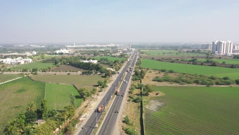 The-drone-camera-is-moving-to-the-side-where-many-cars-trucks-bikes-are-driving-and-a-large-complex-with-fields-and-residential-houses-is-visible-around