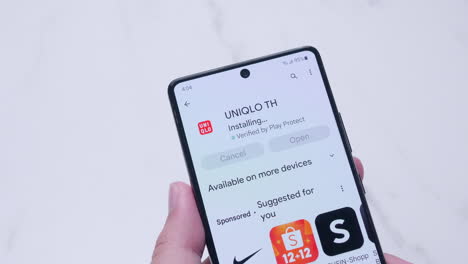 Hand-Hält-Ein-Smartphone-Mit-Der-Installation-Der-Uniqlo-Anwendung-Aus-Dem-Google-Play-Store