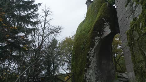 Alte-Architektonische-Struktur-Mit-Großen-Felsen,-Die-Den-Eingang-Eines-Katholischen-Klosters-Mit-Einem-Christlichen-Kreuz-Zeigen,-Umgeben-Von-Großen-Bäumen-Und-Natur