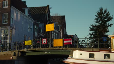 View-from-Amsterdam-canal,-houseboat,-bridge-with-bicycles-and-typical-houses