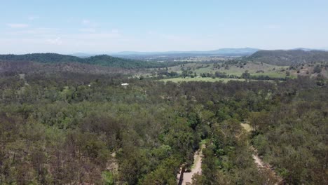 Aerial-view-of-a-forest-showing-mountains-and-a-green-field-with-a-private-house-in-the-background