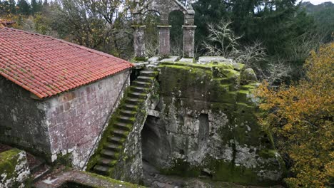 Aerial-drone-shot-of-a-beautiful-old-building-showing-the-exterior-stairs,-a-roof-and-a-high-Christian-cross-of-a-monastery