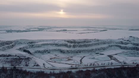 Vista-Aérea-De-Una-Cantera-Cubierta-De-Nieve-En-Una-Noche-De-Invierno-Con-El-Sol-Asomando