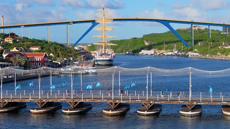 Blaue-Flaggen-Vom-Marathon-Wehen-Im-Wind-Auf-Der-Königin-Emma-Brücke,-Während-Ein-Großes-Mastschiff-Im-Hafen-Vor-Der-Königin-Juliana-Brücke-Liegt