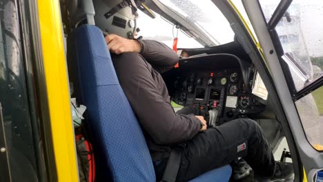 Young-Emergency-Health-Helicopter-Pilot-Prepares-Fastening-Seatbelts-Inside-Cabin-To-Start-Quick-Takeoff-On-A-Rainy-Day,-Shot-Blocked-Traveling-Backwards,-Santiago-de-Compostela,Galicia,Spain