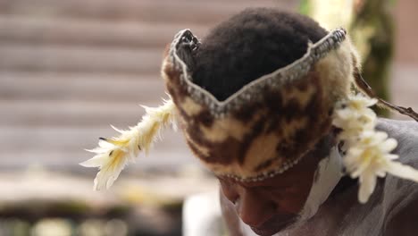 an-old-man-wearing-traditional-Papuan-clothing-is-carving-a-wooden-carving-typical-of-the-Asmat-art-of-Papua,-Indonesia