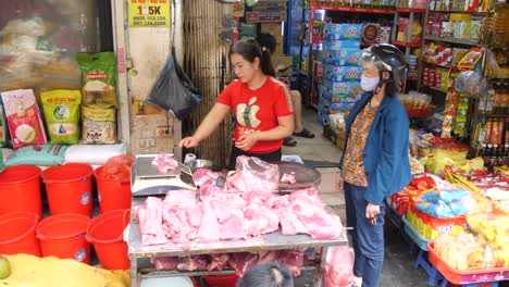 El-Vendedor-Del-Mercado-Húmedo-Corta-Y-Pesa-La-Carne-Para-El-Cliente-Que-Espera-En-Un-Puesto-Concurrido