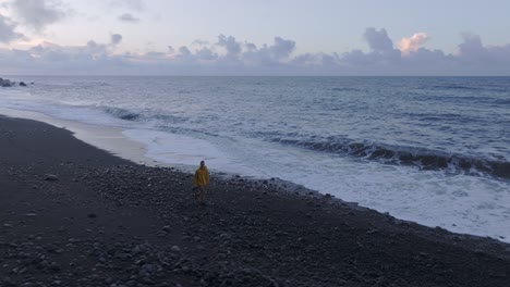 Luftschwenk-Mit-Drohne-Auf-Einen-Jungen-Mann,-Der-Bei-Sonnenaufgang-Am-Strand-Spaziert,-Azoren