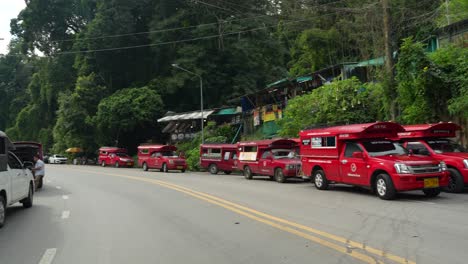 Lange-Reihe-Geparkter-Roter-Songthaew-Transporter-Entlang-Einer-Dschungelstraße