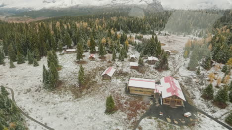 Vista-Aérea-Filmada-Desde-Un-Helicóptero-Volando-Que-Muestra-Un-Vibrante-Y-Nevado-Campo-Salvaje,-Cabañas-Y-Montañas-Circundantes-Cubiertas-De-Nieve.