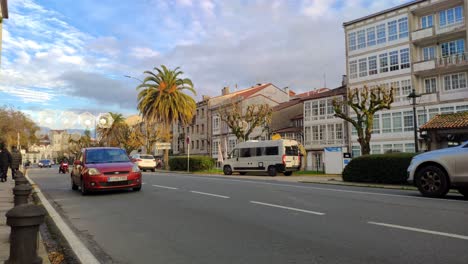 Vehículos-Con-Motor-De-Combustión-Conduciendo-Por-Una-Avenida-De-La-Ciudad-Con-Palmeras-En-Un-Frío-Día-De-Invierno-Con-Nubes-En-El-Cielo,-Disparo-Bloqueado,-Santiago-De-Compostela,-Galicia