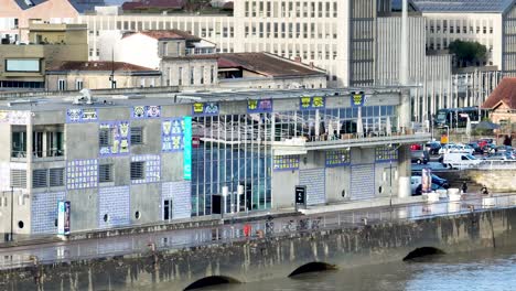 Museo-De-Educación-Infantil-De-Ciencias-De-La-Tapa-En-La-Orilla-Del-Río-Garona-Con-Ciclistas-Pasando,-Tiro-Aéreo-A-La-Derecha