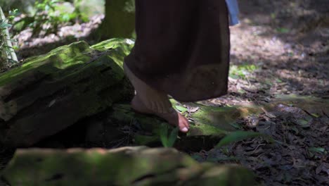 Mujer-Morena-Caminando-Sobre-Las-Piedras-De-Un-Frondoso-Bosque,-Con-Los-Pies-Descalzos-Y-Un-Vestido-Marrón