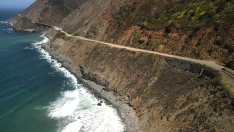 Cinematic,-aerial,-drone-shots-of-the-seaside-in-the-valley-with-a-Ford-Mustang-traveling-on-the-highway