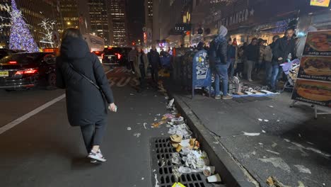 Gente-Caminando-Por-Una-Calle-Llena-De-Basura,-Por-La-Noche,-En-La-Ciudad-De-Nueva-York