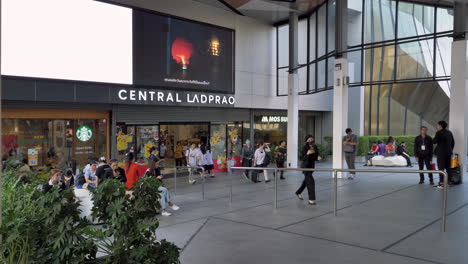 Los-Compradores-Entran-Y-Salen-Del-Centro-Comercial-Central-Ladprao-Mientras-Algunos-Transeúntes-Están-Sentados-En-Los-Bancos-En-La-Entrada-De-Los-Grandes-Almacenes-En-Bangkok,-Tailandia.