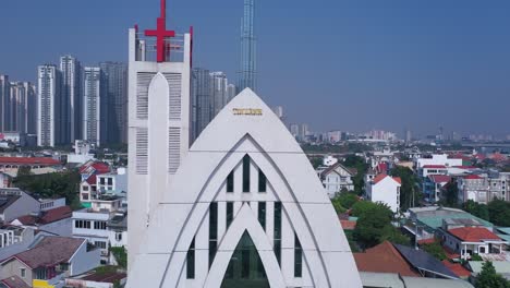 Seltsames-Modernes-Kirchengebäude-Und-Stadtpanorama-An-Einem-Sonnigen-Tag.-Kranaufnahme,-Die-Das-Rote-Kreuz-Und-Hochhäuser-Enthüllt