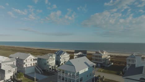 Una-Vista-Aérea-De-Las-Casas-De-Playa-Domina-La-Playa-De-Galveston,-Con-Un-Telón-De-Fondo-De-Cielos-Azules-Y-Nubes-Blancas-En-East-Beach-En-La-Isla-De-Galveston,-Texas.