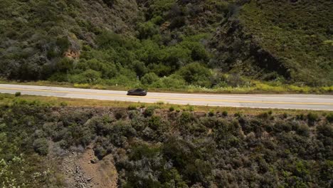 Eine-Filmische-Drohnenaufnahme-Aus-Der-Luft-Eines-Ford-Mustang-Cabrio-Entlang-Des-Tals-Und-Der-Berggipfel