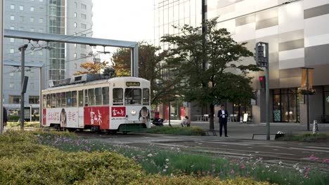 Oldtimer-Straßenbahn-Nähert-Sich-Dem-Bahnhof-Toyama,-Während-Eine-Person-über-Die-Kreuzung-Geht