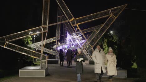 Gente-Paseando-Bajo-Una-Enorme-Estrella-Adornada-Con-Luces-Festivas-En-El-Parque-Durante-El-Día-Nacional-De-Galati-En-Rumania---Plano-Amplio