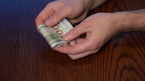 Hands-counting-400-USD-and-folding-into-hand-above-wooden-table,-close-up