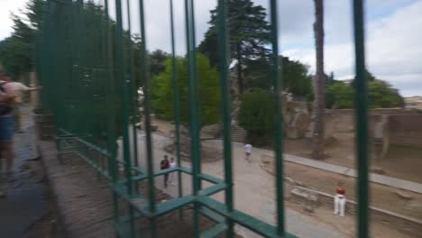 Rome-Immersive-POV:-Moving-In-Busy-Streets-to-Chiesa-Santi-Luca-e-Martina,-Italy,-Europe,-Walking,-Shaky,-4K-|-Tourists-Sitting-In-Ruins-Through-Gate