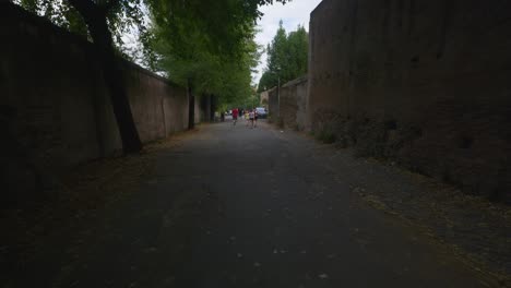 Rome-Immersive-POV:-Moving-In-Busy-Streets-to-Chiesa-Santi-Luca-e-Martina,-Italy,-Europe,-Walking,-Shaky,-4K-|-Tourists-Walking-Along-Dark-Path