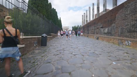 Rome-Immersive-POV:-Moving-In-Busy-Streets-to-Chiesa-Santi-Luca-e-Martina,-Italy,-Europe,-Walking,-Shaky,-4K-|-Couple-In-Crowd-Near-Old-Ruins