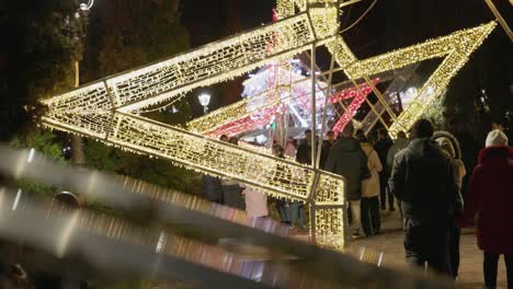 Gente-Paseando-Bajo-La-Gran-Estrella-Adornada-Con-Luces-Vibrantes-En-El-Parque-Como-Parte-De-Las-Festividades-Del-Día-Nacional-De-Galati-En-Rumania---Plano-Medio