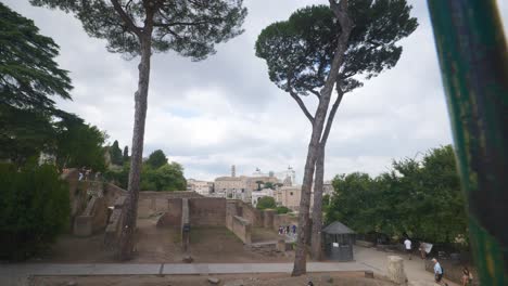 Rome-Immersive-POV:-Moving-In-Busy-Streets-to-Chiesa-Santi-Luca-e-Martina,-Italy,-Europe,-Walking,-Shaky,-4K-|-Looking-At-Ruins-Through-Metal-Gate