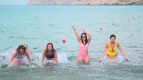 Grupo-De-Amigos-Divirtiéndose-Chapoteando-Aguas-De-Playa-Con-Anillos-De-Natación-En-Verano,-Cámara-Lenta