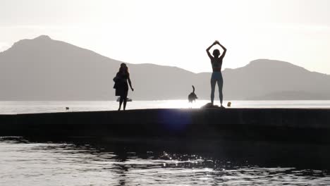 As-sunrise-adorns-Port-de-Pollenca's-coast,-a-dog-joyfully-approaches-a-woman-exercising-joga-on-a-pier,-mistaking-her-for-his-owner