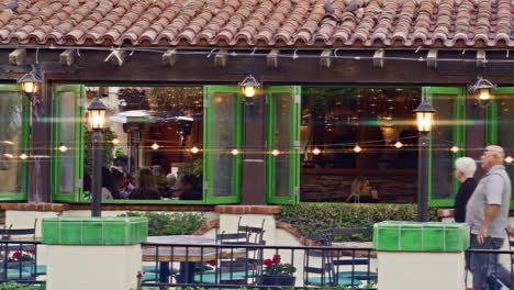 Wide-stable-shot-of-people-eating-at-a-restaurant-in-downtown-Palm-Springs,-California-with-pedestrians-walking-by-and-lens-flare-effect